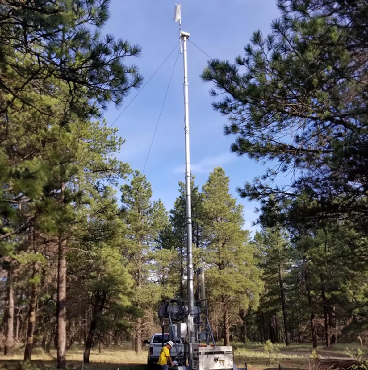 Cell on Wheels (COW) mobile cellular unit deployed in a forest clearing with a technician - emergency network deployment in a remote location